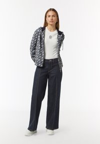 Gevoerde jas met een navy en wit patroon, witte geribbelde t-shirt en donkerdenim wijde broek met zichtbare stiksel details.