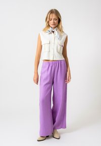 Vit ärmlös cropped topp med två framfickor, ihopparad med ljuslila vida byxor. Slät tyg och avslappnad passform. Ljust färgad fotbeklädnad.