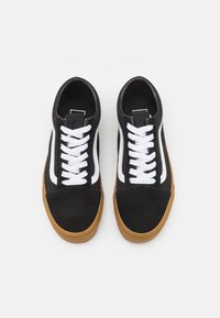 Svarta mockaskor med vita snören och sidostrecker, med en sula i gummigummi och rundad tådesign.