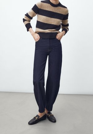 Gestreepte trui in bruin en zwart, gecombineerd met een donkerdenim wijde broek en zwarte instappers met gouden hardware accenten.