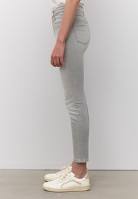 Jeans skinny gris claro con una cintura de altura media, diseño minimalista y un desvanecimiento sutil. Combinados con zapatillas blancas con acentos beige.