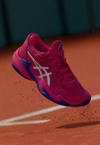 Asics tenisa apavu iezīme ir spilgti rozā acs augšdaļa, balts logo, zili akcenti un teksturēta zole ar dinamisku formu.
