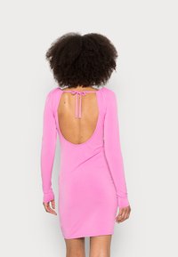 Vestido rosa de mangas longas com uma silhueta ajustada, design de costas abertas e fecho com laço no pescoço. Tecido suave e elástico.
