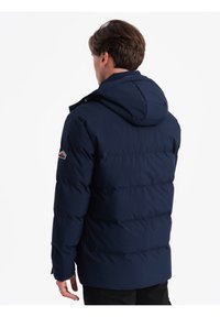 Námořnická puffer bunda s kapucí, která má prošívaný design, elastické manžety a logo nášivku na levém rukávu. Vyrobena z hladkého, voděodolného materiálu.