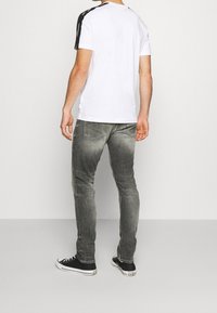 Vit t-shirt med svarta axeldetaljer, kombinerad med grå jeans. Svarta sneakers fulländar den avslappnade outfiten. Fokus på sportiga designelement.