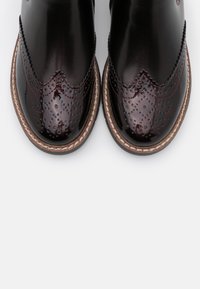 Brune læder ankelstøvler med en poleret overflade, dekorativ brogue-detaljering og en kontrastsyet sål. Rund tåform.