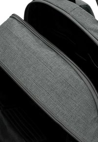 Intérieur d'un sac à dos en tissu gris avec un rabat texturé, fermeture éclair et doublure noire. Dispose de compartiments pour l'organisation et le rangement.