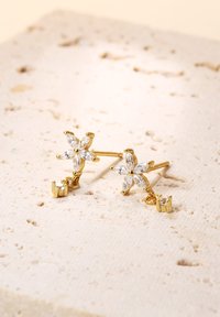 Pendientes en forma de flor de oro con piedras claras en corte marquesa, con un pequeño detalle de gema colgante en uno de los pendientes.