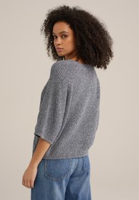 Grå stickad tröja med lös passform, vid halsringning och trekvartslånga ärmar. Matchad med ljusblåjeans.