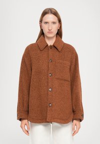 Giacca oversize in misto lana marrone con colletto, chiusura frontale con bottoni, taschino sul petto e tessuto testurizzato. Progettata con maniche morbide.