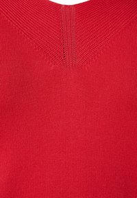 Pull-over en tricot rouge avec un col en V texturé, une surface lisse et des accents côtelés le long de l'encolure et des épaules.