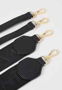 Črne torbe z naramnicami iz teksturirane usnje in tkanine. Tri naramnice imajo zlate sponke z blagovno znamko in se razlikujejo po dolžini.