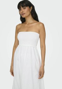 Vestido blanco sin mangas con un cuerpo fruncido, falda fluida y una tela texturizada. Presenta una parte superior ajustada y una parte inferior suelta.