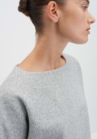 Grijze sweatshirt met een gestructureerde afwerking, brede halslijn en losse pasvorm. De stof lijkt zacht en licht gemêleerd.