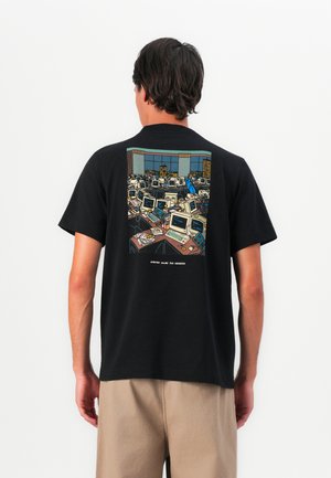 Man wearing black t-shirt with graphic of crowded office filled with retro computers and a person in blue walking through desks.