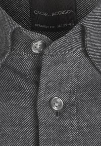 Camicia grigia a fantasia con vestibilità dritta, texture intrecciata e bottoni metallici. Etichetta con la scritta "Oscar Jacobson, M 39-40."