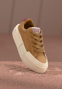 Světlé semišové tenisky s bílou robustní podrážkou, se šněrováním a tmavorudým štítkem s logem "Converse All Star". Výrazné detaily prošívání.