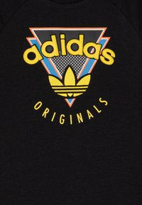 Črna majica s kapuco z večbarvnim grafičnim motivom, ki vsebuje rumeno besedilo "adidas" in "ORIGINALS" ter rumenim trefoil logotipom na dnu.