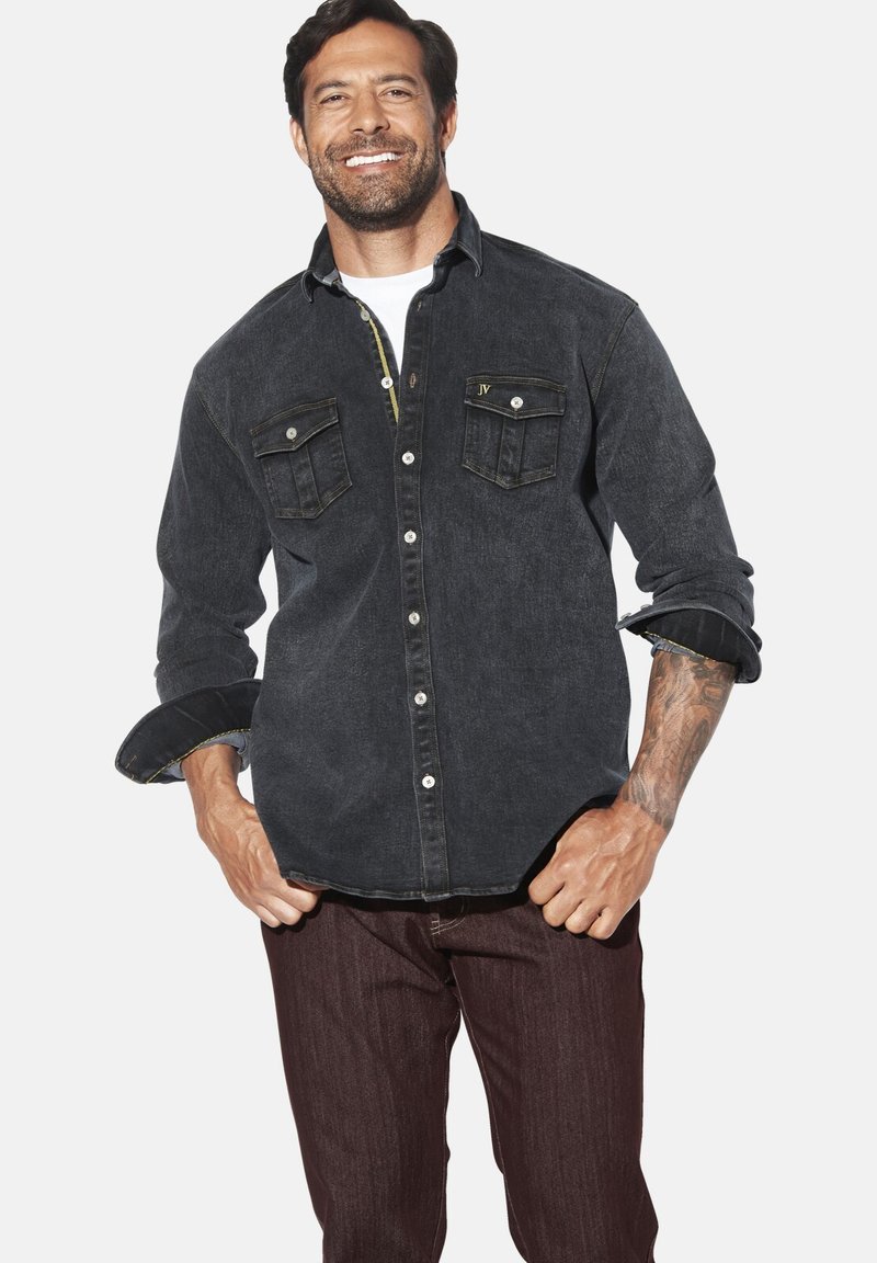 Dunkelblaues Denim-Hemd mit zwei Brusttaschen, hochgekrempelten Ärmeln und kontrastierenden Nähten. Getragen mit dunklen Hosen.
