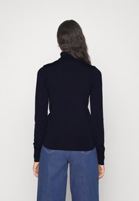 Laivaston sininen pooloneule, joissa pitkät hihat, resorit hihansuissa ja helmassa, sileä pinta, yhdistetty leveälahkeisiin sinisiin farkkuihin.