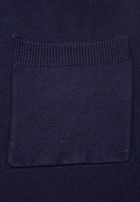Gros plan sur une poche de pull tricoté bleu foncé avec bord supérieur côtelé et tissu tricoté texturé.