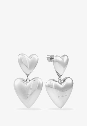 Une paire de boucles d'oreilles pendantes en argent brillant en forme de double cœur, avec "CPH STUDIOS" gravé sur les cœurs les plus grands, présentée sur fond blanc.