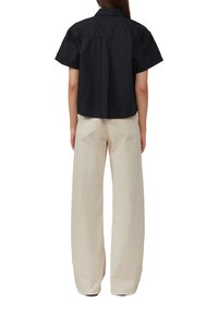 Chemise noire à manches courtes avec col, associée à un pantalon beige taille haute à jambes larges. Texture de tissu lisse, detailing minimal.
