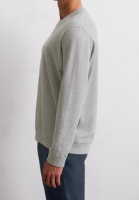 Sudadera gris con cuello redondo, mangas largas y puños acanalados. Confeccionada en una tela suave, presenta un corte recto y un diseño minimalista.