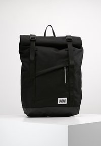 Mochila negra de tipo roll-top, fabricada en tejido resistente, con correas ajustables, un bolsillo frontal con cremallera y una base de goma con detalle del logo.