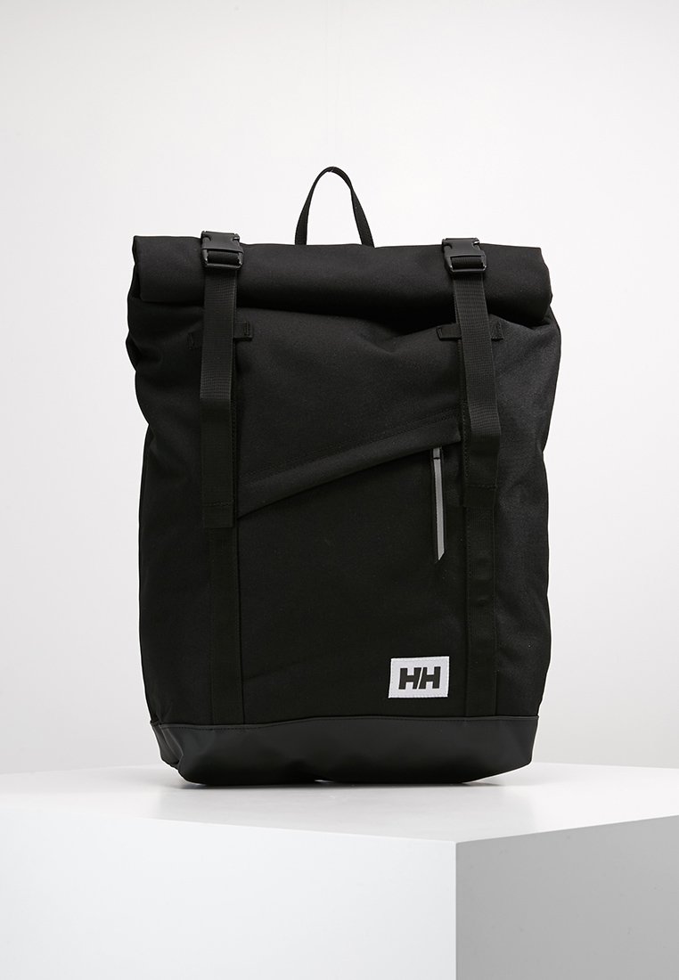 Mochila negra de tipo roll-top, fabricada en tejido resistente, con correas ajustables, un bolsillo frontal con cremallera y una base de goma con detalle del logo.