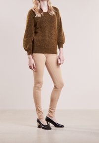 Brun fluffig tröja med ballongsärmar, i kombination med beiga tighta byxor och svarta klackar med en chunky klackdesign. Enkel bakgrund.