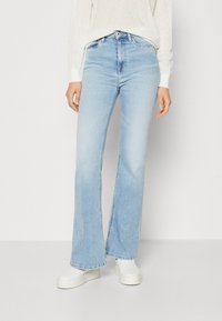 Ljusblå bältesjeans i denim med hög midja, fem fickor och subtila blekningar. Matchas med vita skor.