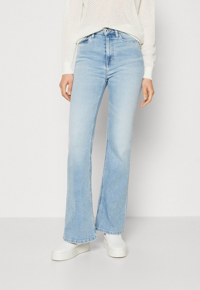 Ljusblå bältesjeans i denim med hög midja, fem fickor och subtila blekningar. Matchas med vita skor.