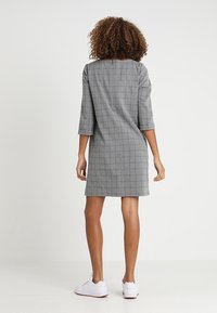 Vestido a cuadros grises con mangas de tres cuartos, un ajuste relajado y un dobladillo que cae por encima de la rodilla. Combinado con zapatillas blancas.