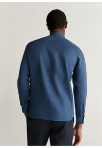 Koszula z długim rękawem w ciemnoniebieskim materiale, z kołnierzykiem zapinanym na guziki oraz mankietami na guziki. Charakteryzuje się gładką fakturą i tylnym karczkiem.