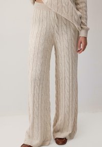 Veyleikinn leve-leg buksot i ljósbeigju lit, með áferðarklæddri mynstri, ribbaða mitti og afslappaðri pasjót. Mjúkur prjónað efni.