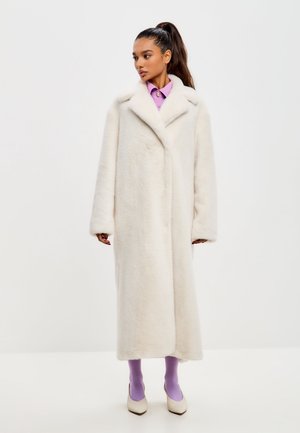 Cappotto lungo color crema con una finitura morbida e testurizzata, ampio colletto a punta e maniche oversize. Presenta una chiusura con bottoni e un orlo di lunghezza media.