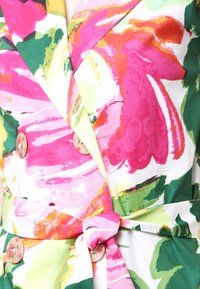 Kukkakuosiset mekko pastelliväreissä, joissa on vaaleanpunaisia, vihreitä ja keltaisia kuvioita. Suunniteltu kietoutuvaksi nauhalla, suurilla napituksilla ja pehmeällä kankaan tekstuurilla.