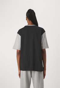 Černošedé tričko s krátkým rukávem, směs bavlny, s kontrastními rukávy a kulatým výstřihem; nošené s odpovídajícími šedými kalhotami.