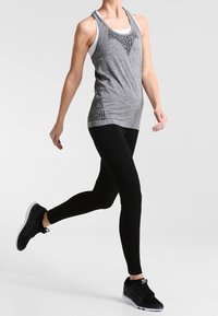 Top sportivo grigio con accenti neri a motivi, abbinato a leggings neri e sneaker nere, che mette in evidenza un design aderente e un tessuto elasticizzato.