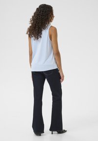 Gaiši zila bez piedurknēm blūze, apvienota ar tumši ziliem platām džinsiem. Gluda auduma tekstūra ar smalkiem šuvju detaļām, valkāta ar melniem augstpapēžu apaviem.