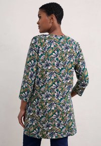 Kwiatowa tunika z zielonym tłem i białymi, fioletowymi oraz żółtymi wzorami kwiatów. Posiada rękawy o długości trzech czwartej i luźny krój.