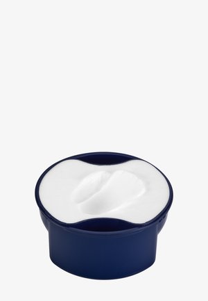 Okrągłe, granatowe opakowanie wypełnione białym kremem. Powierzchnia jest gładka z lekkim wgłębieniem, co wskazuje na użycie produktu.