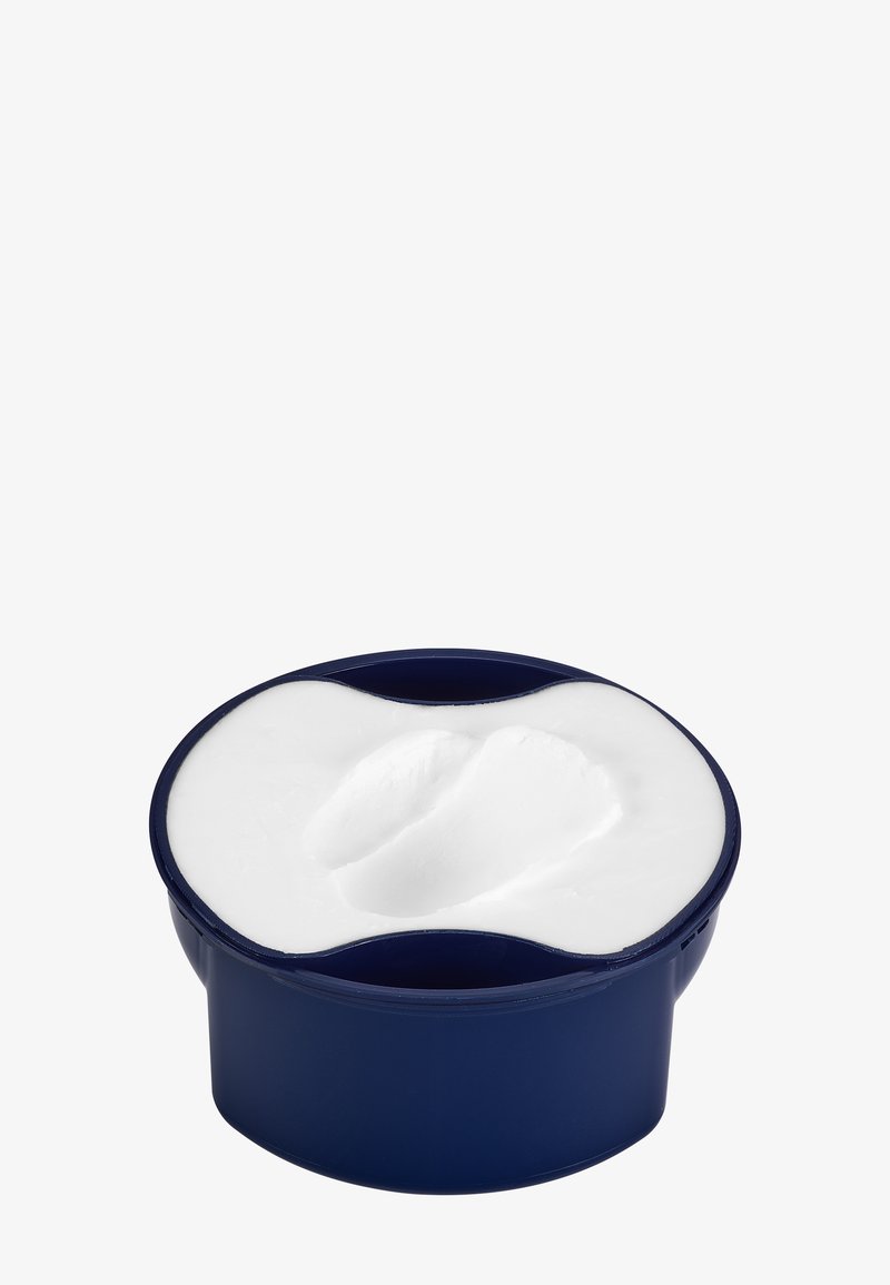 Okrągłe, granatowe opakowanie wypełnione białym kremem. Powierzchnia jest gładka z lekkim wgłębieniem, co wskazuje na użycie produktu.