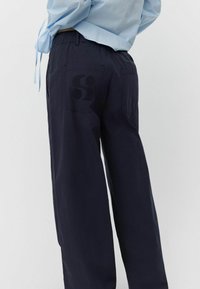 Marineblaue weit geschnittene Hosen aus leichtem Stoff, mit einem elastischen Bund und einem großen geprägten Logo auf der Gesäßtasche.