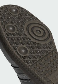 Mörk gummisula med ett geometriskt strukturerat mönster, cirkulära och upphöjda inslag, samt distinkta triangulära och runda greppdesigns.