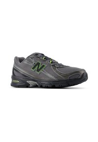 Γκρι και μαύρο αθλητικό παπούτσι New Balance με πράσινες πινελιές και πανί πάνω μέρος, εμφανιζόμενο από το πλάι σε λευκό φόντο.