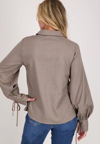 Bruine gestreepte blouse met een kraag, ballonmouwen en strikdetails bij de manchetten. Draagt bij blauwe jeans, met een relaxte pasvorm.