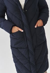 Mornarska puffer jakna s dva bočna džepa, kaput s prešanim dizajnom i zatvaranjem na munju. Ima mekani, teksturirani materijal i ležeran kroj.