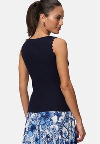 Débardeur côtelé bleu marine avec des bords festonnés, associé à une jupe à motif floral bleu et blanc, avec une coupe ajustée.
